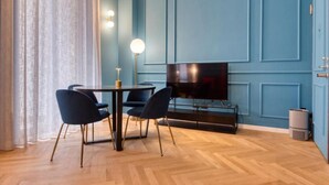 A modern living room with a blue wall, a flat-screen TV, a round dining table with chairs, and a floor lamp. - VivimiHome-Suite Topazio, Luxury Apartment (Milan)