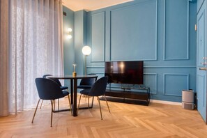 A modern living room with a blue wall, a flat-screen TV, a round dining table with chairs, and a floor lamp. - VivimiHome-Suite Topazio, Luxury Apartment (Milan)