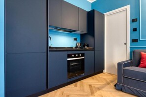 A compact kitchen with dark cabinetry, a built-in oven, and a countertop with a kettle. - VivimiHome-Suite Topazio, Luxury Apartment (Milan)
