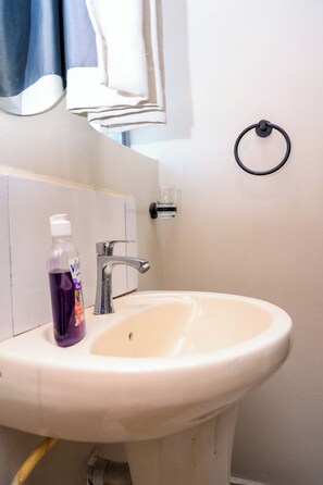 A bathroom with a white sink, a mirror, a towel rack, and a bottle of liquid soap. - Cosy 1 Bedroom Apartment Near JKIA Airport Nairobi (Nairobi)