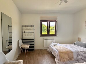 A bedroom with a bed, a chair, a radiator, and a window with a view of greenery. - La Casa de Ruri 5926 Lodging (Isla)