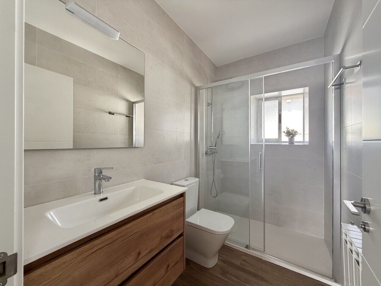 Un baño moderno con ducha envuelta en vidrio, tocador de madera y un espejo grande.