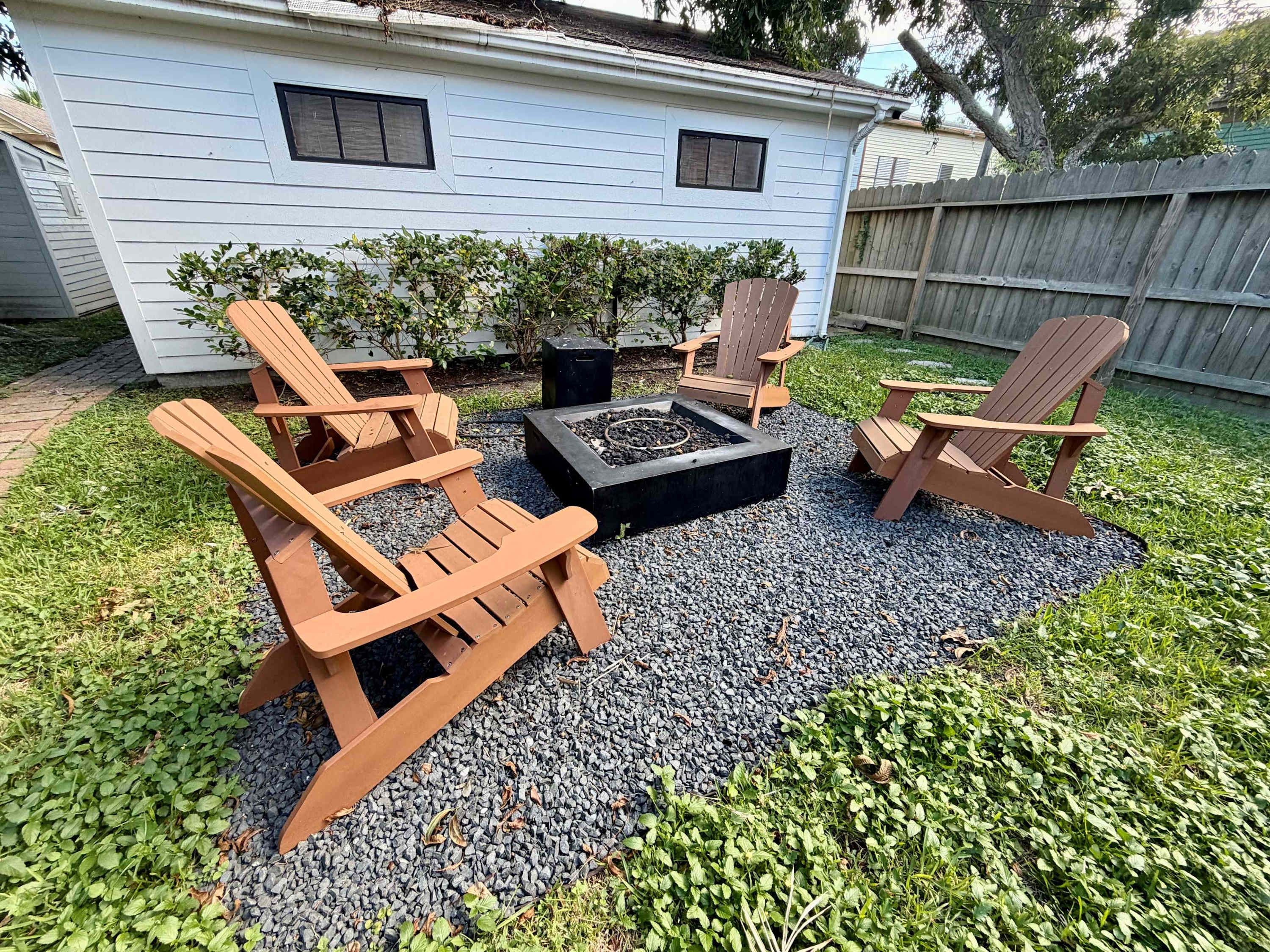 A backyard with a fire pit, wooden Adirondack chairs, and a gravel patio.