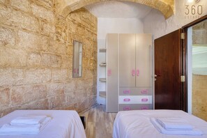 A hotel room with stone walls, a wardrobe with pink handles, and two beds. - 3BR Townhouse with Private Pool & BBQ in Birkirkara (Birkirkara)