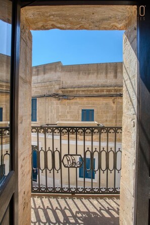 Ein Balkon mit schmiedeeisernem Geländer und Blick auf Häuser mit blauen Fensterläden.