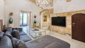 A living room with a sofa, a coffee table, a TV mounted on a stone wall, and a wooden door. - 3BR Townhouse with Private Pool & BBQ in Birkirkara (Birkirkara)