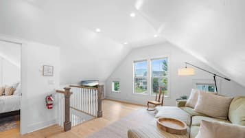 A spacious attic bedroom with a large window, a wooden staircase, and a cozy seating area with a sofa and cushions.
