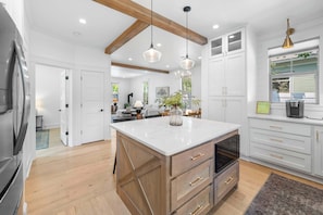 A modern kitchen with a large island, wooden cabinetry, and pendant lighting.