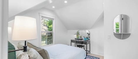 A bedroom with a bed, a desk, a chair, a lamp, a window, and a mirror.