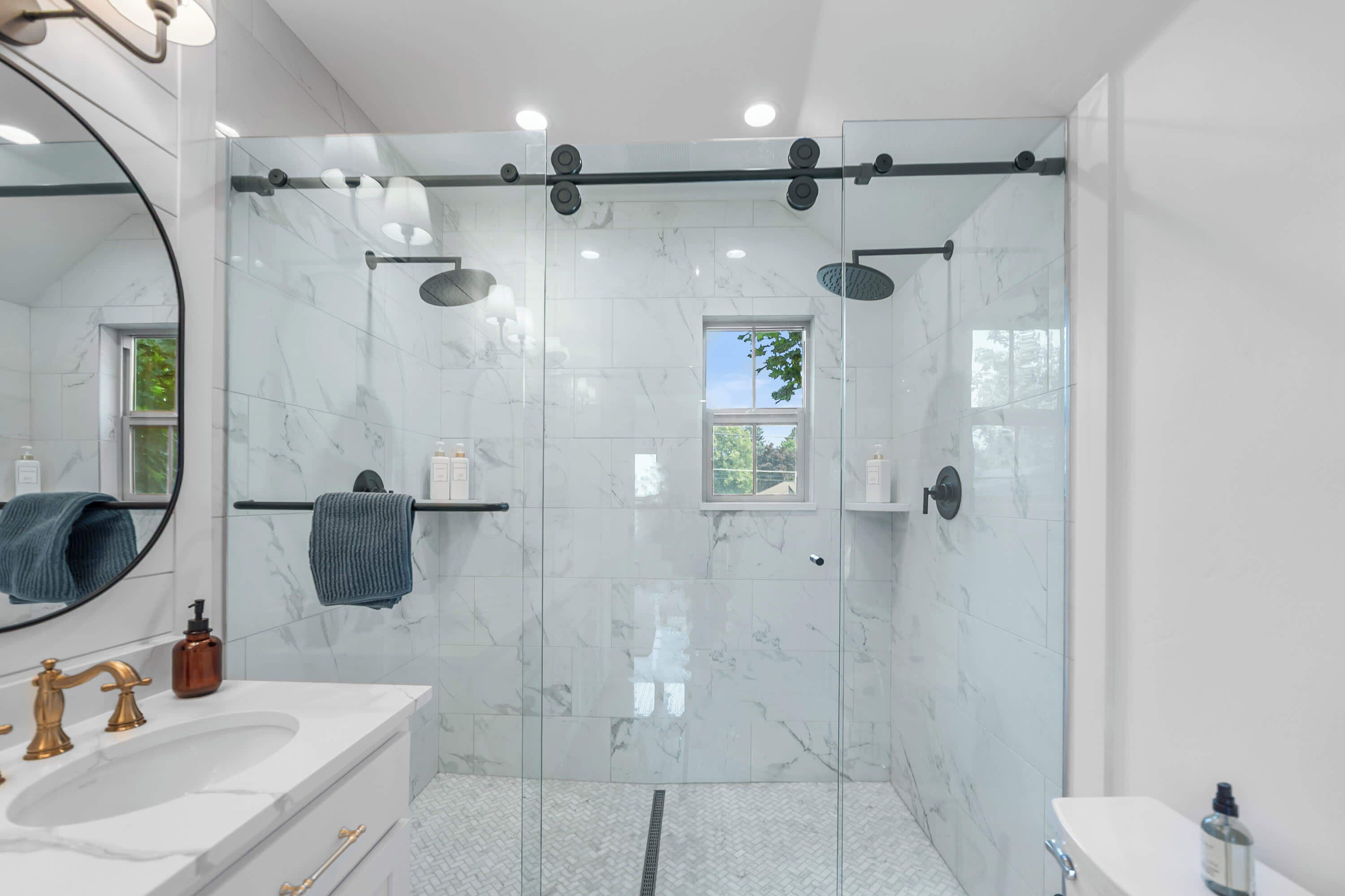 A modern bathroom with a glass shower enclosure, a large mirror, and a marble-tiled wall.