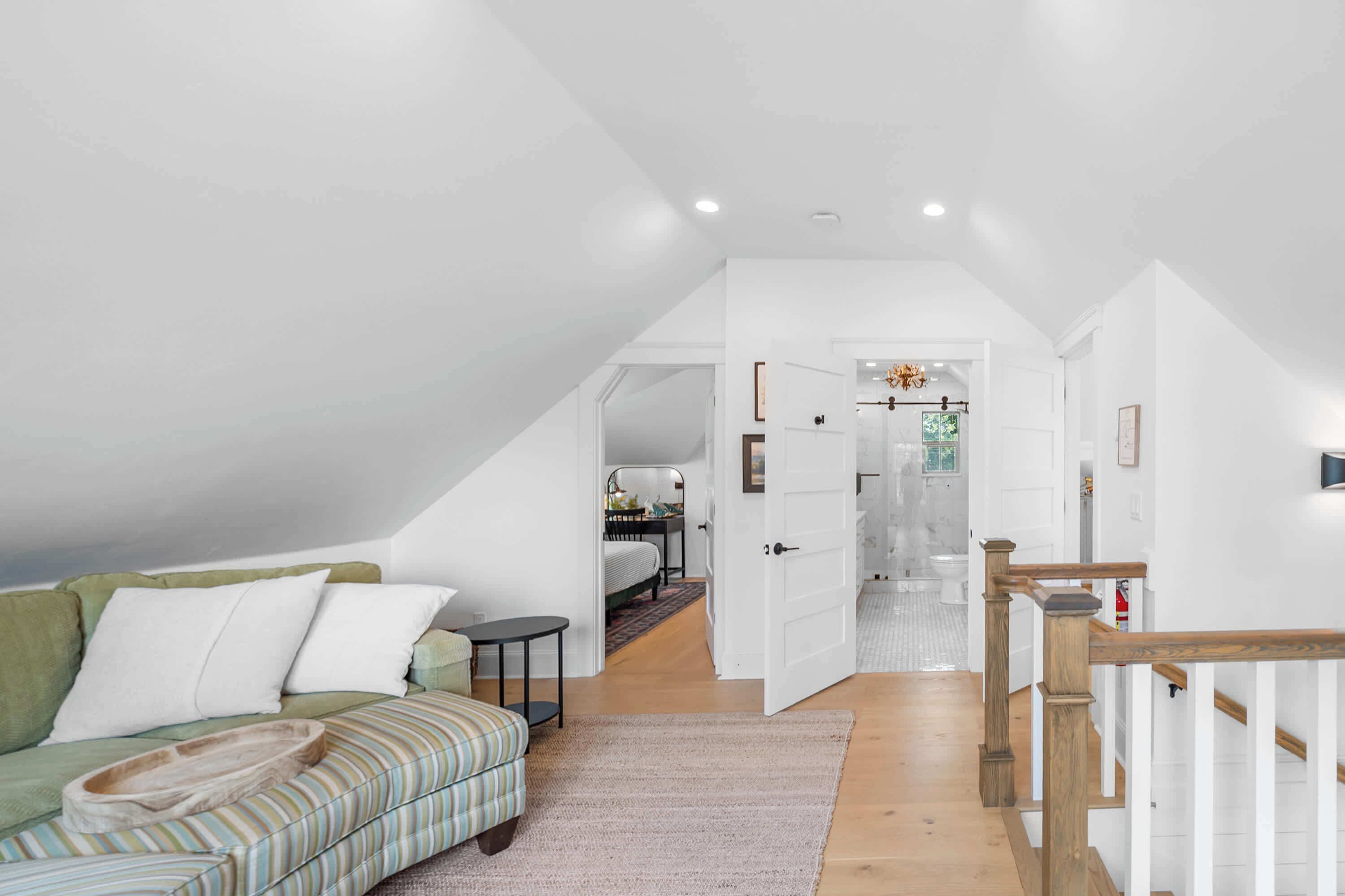 Une chambre spacieuse aménagée en mezzanine, avec un plafond haut, un lit intégré, un petit coin salon et une vue sur la salle de bain.