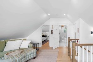 A spacious loft bedroom with a high ceiling, a built-in bed, a small seating area, and a view of the bathroom.