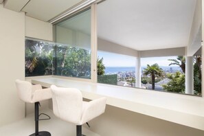 A modern room with a large window, two white chairs, and a view of a cityscape and greenery. - Fresnaye Villa, Moroccan Escape & Two Pools (Cape Town)