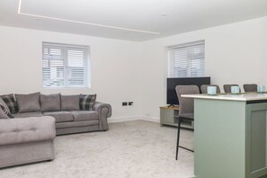 Ein modernes Wohnzimmer mit einem grauen Sofa, einem Fernseher und einem kleinen Tisch mit Tassen.