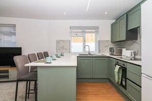 A compact kitchen with a central island, a built-in oven, and a microwave. - Greenswood Mews (Brixham)