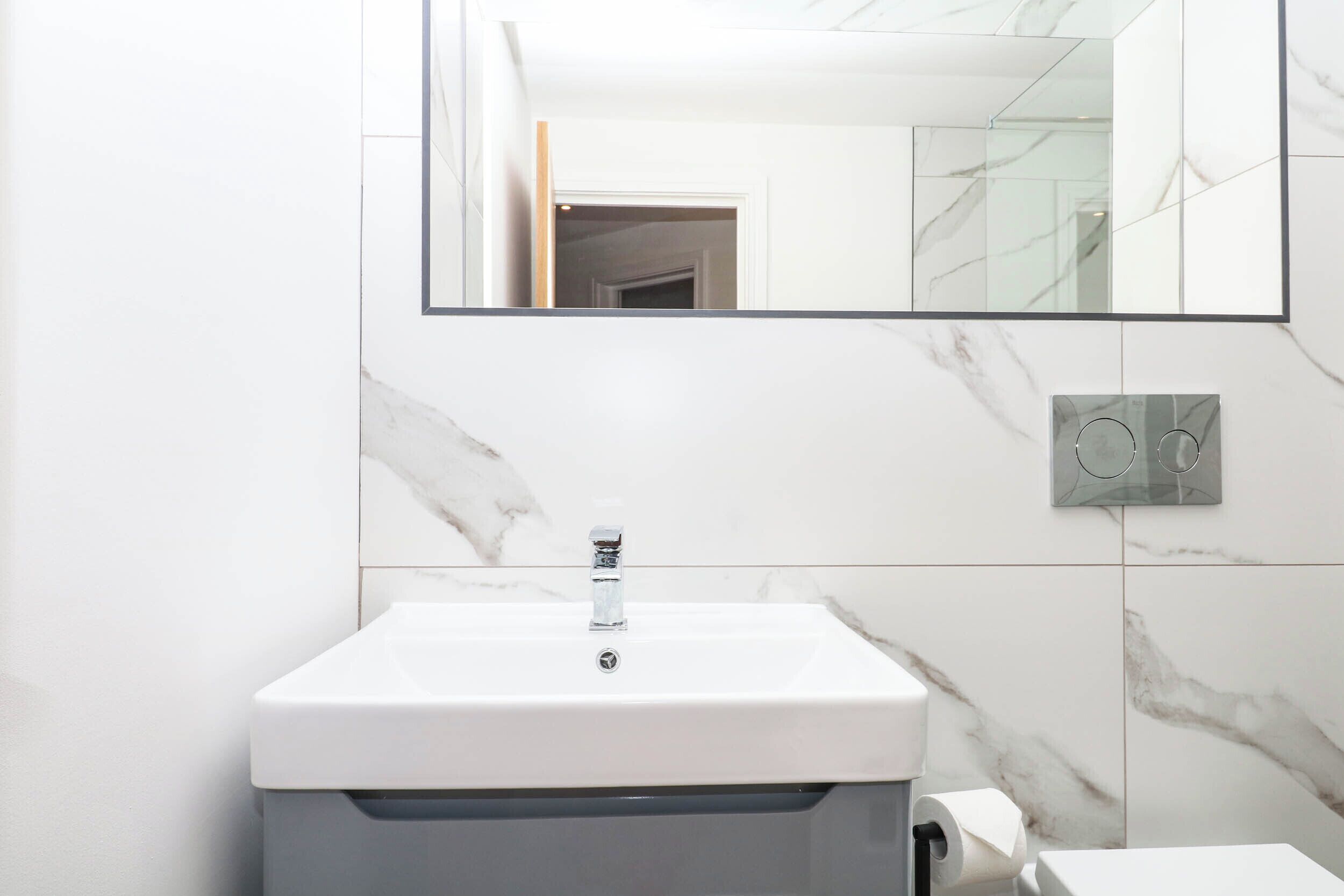 Un baño con un lavabo blanco, un espejo y paredes con diseño de mármol.