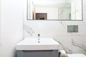 Ein Badezimmer mit einem weißen Waschbecken, einem Spiegel und Wänden mit Marmoroptik.