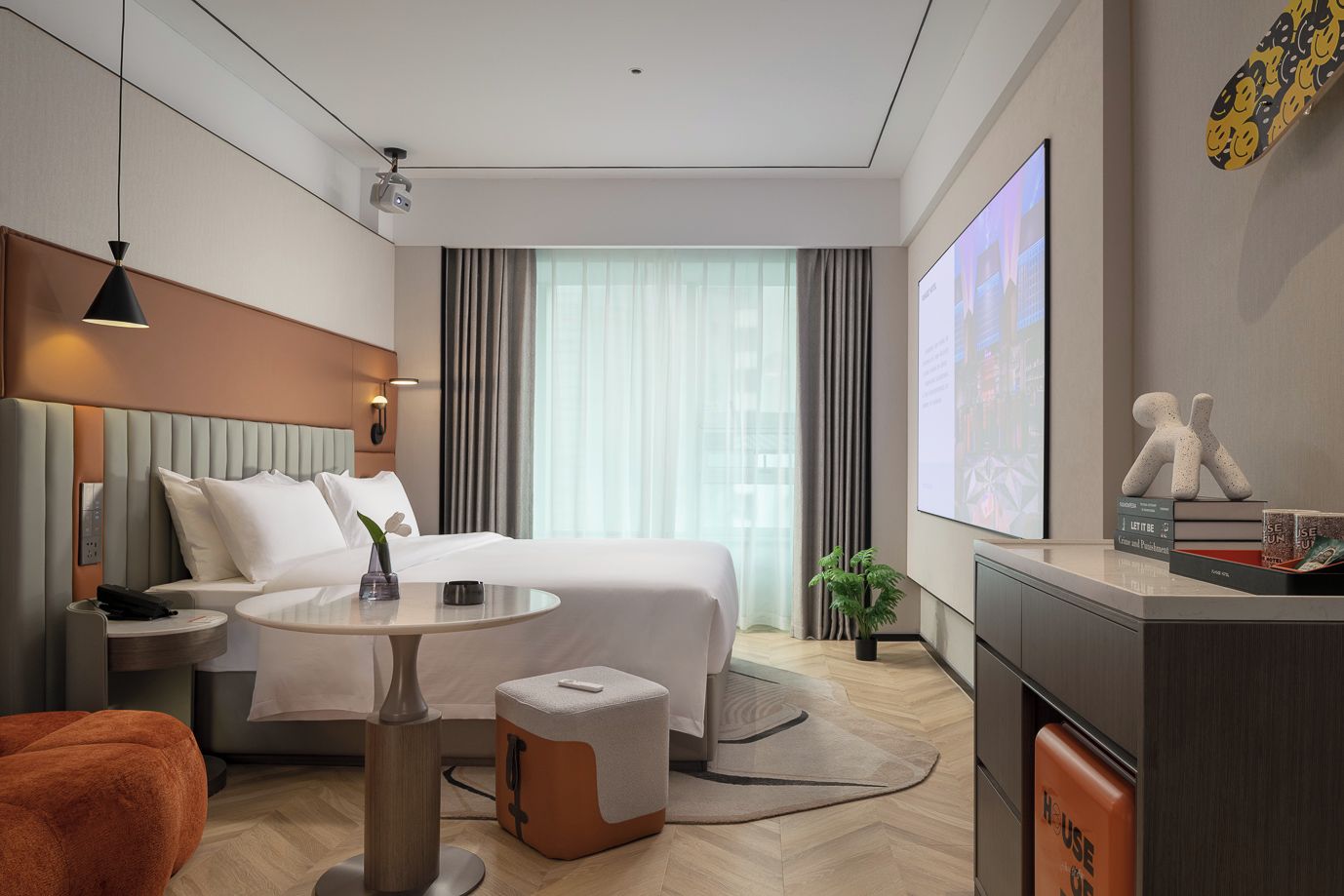 Una habitación de hotel moderna con una cama, una mesita de noche, una lámpara y una pequeña mesa redonda.