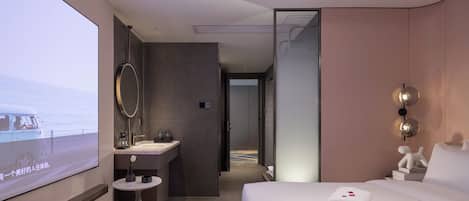 A hotel room with a bed, a bedside table, a mirror, a sink, and a television screen.