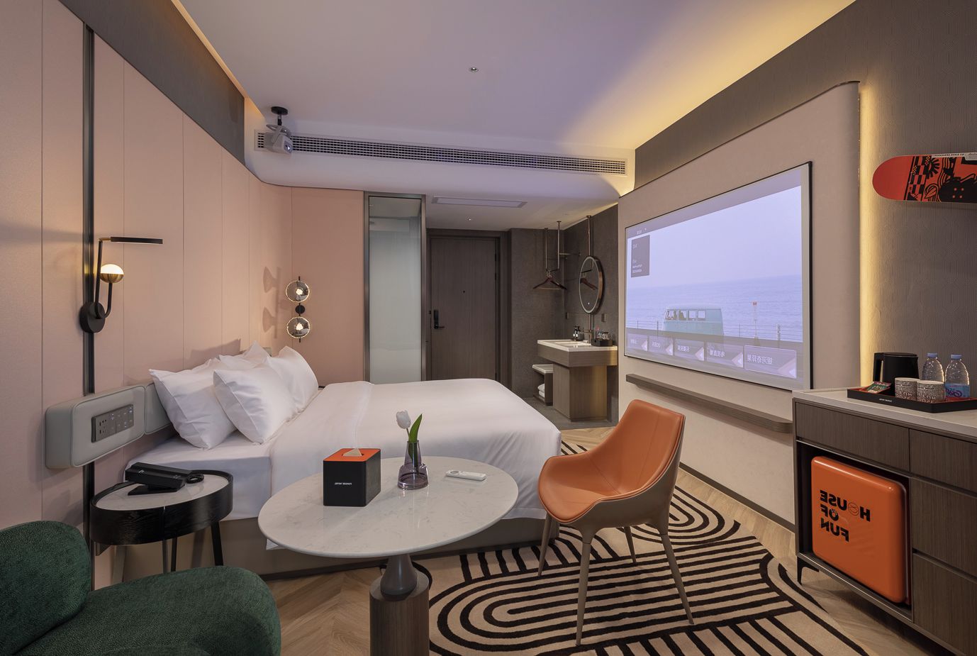 Habitación de hotel con cama, mesita de noche, silla, escritorio y una gran pantalla de televisión.