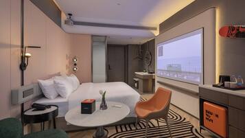 Habitación de hotel con cama, mesita de noche, silla, escritorio y una gran pantalla de televisión.