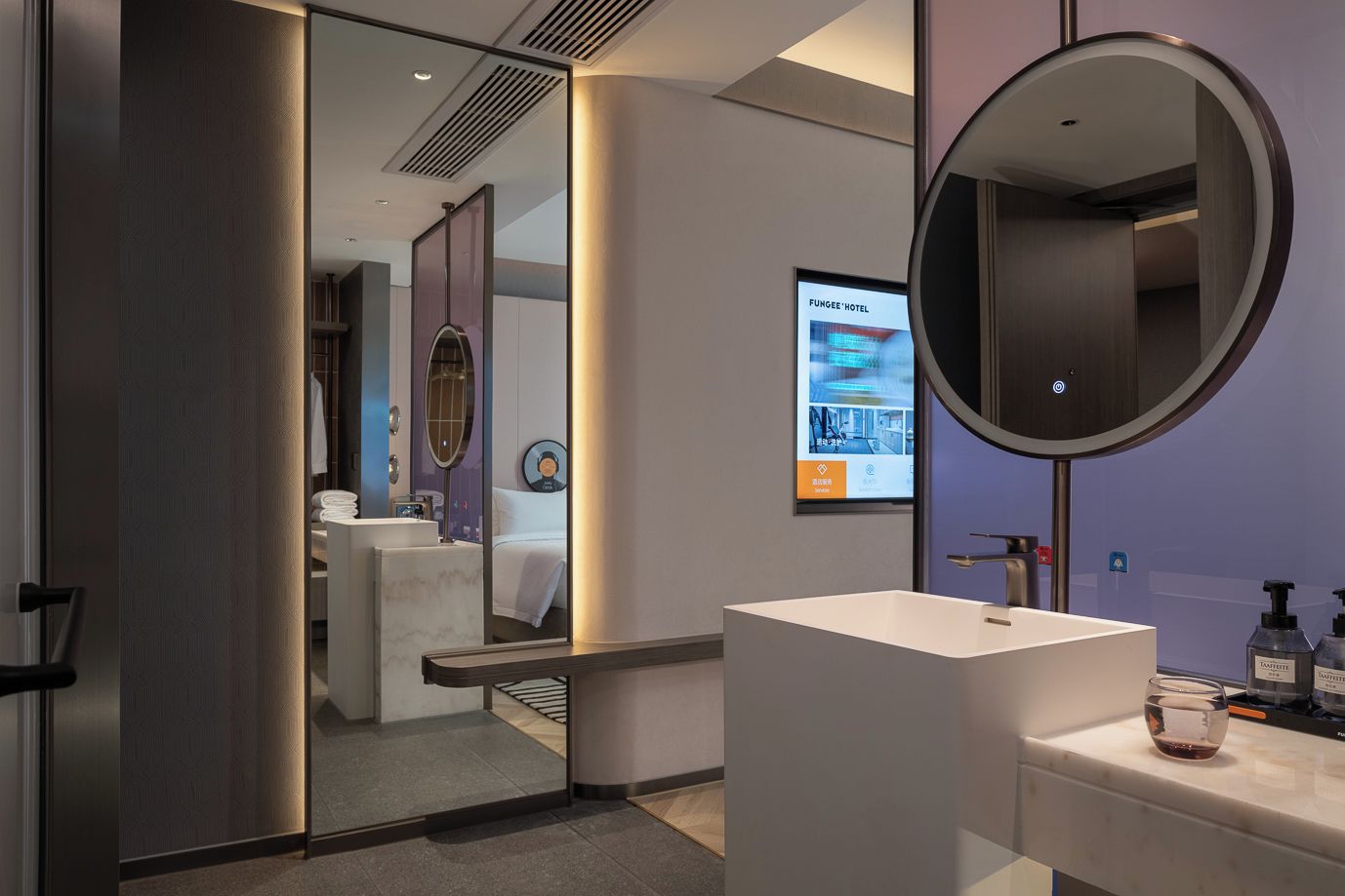A modern hotel bathroom with a large mirror, a white sink, and a digital screen displaying hotel information.