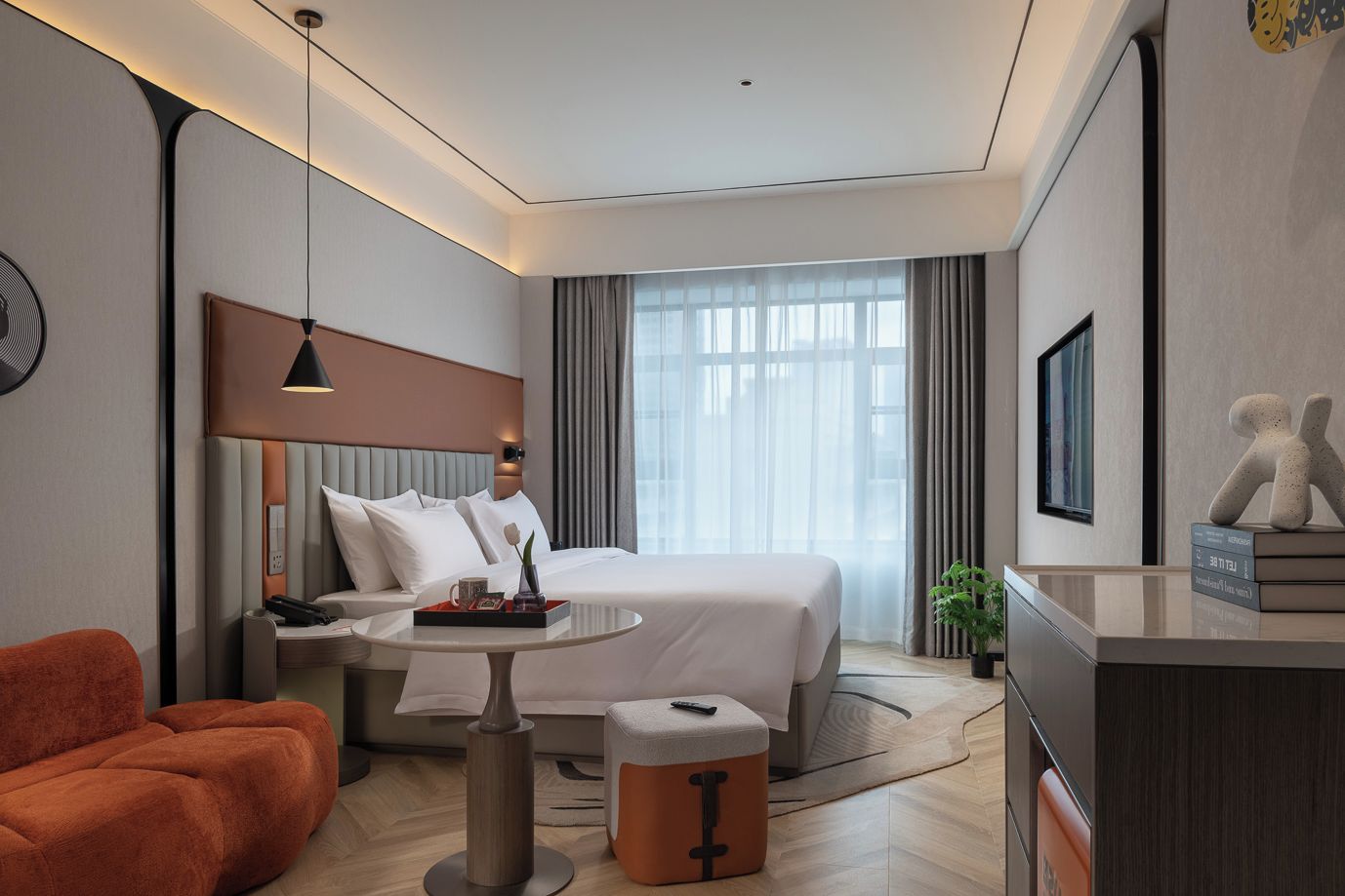 Ein modernes Hotelzimmer mit einem Bett, einem Schreibtisch, einem Sessel, einem Couchtisch und einer Pflanze.