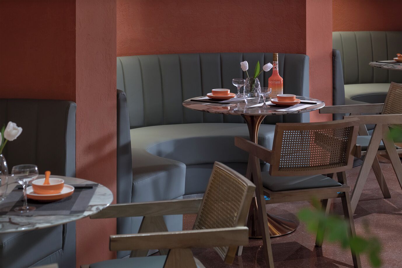 Un interior de restaurante con cabinas, mesas redondas y sillas de mimbre.