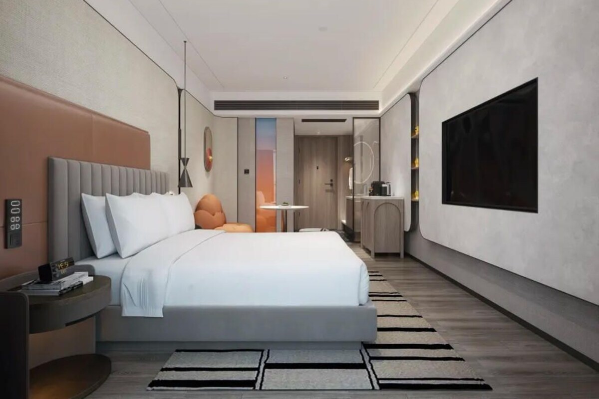 A modern hotel room with a large bed, bedside tables, a desk, and a television.