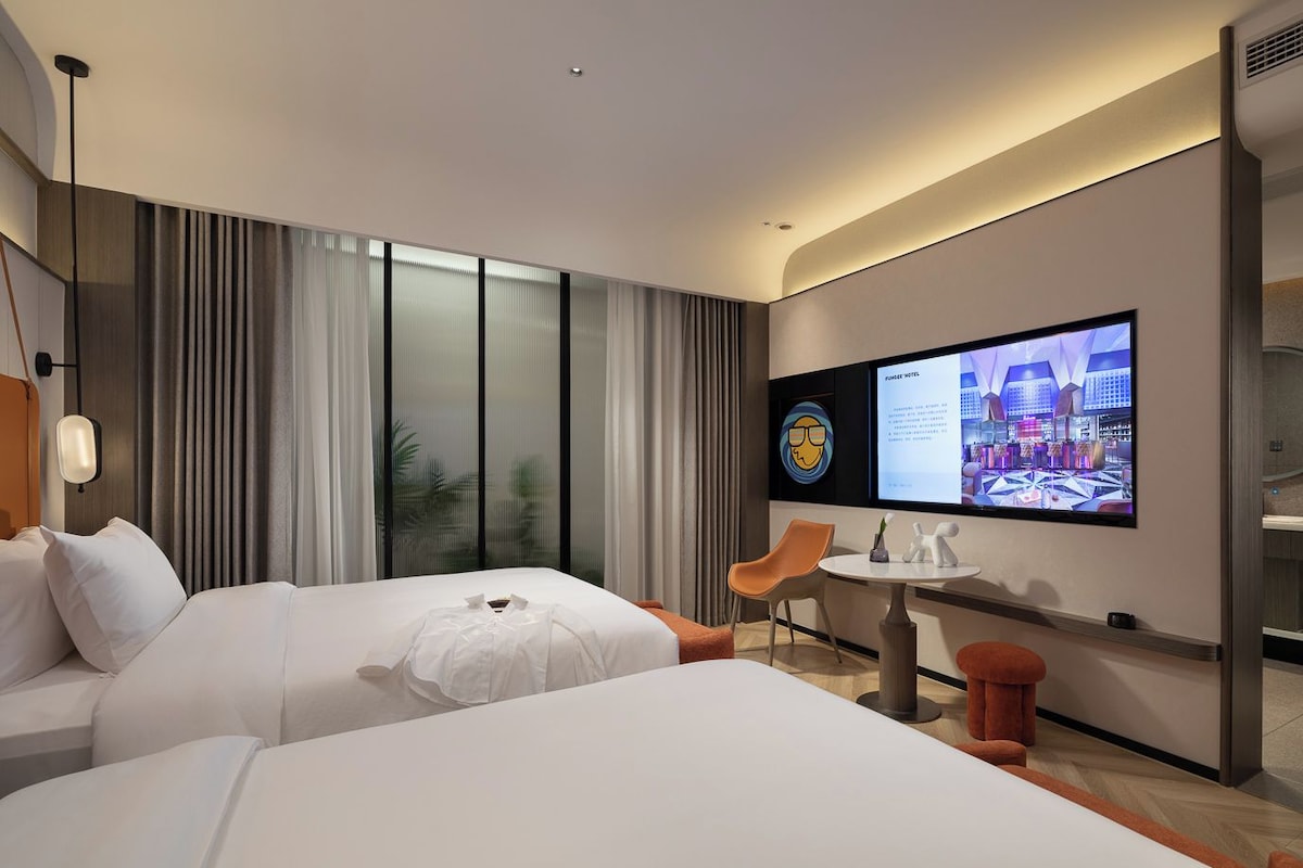 A hotel room with two beds, a TV, a small table, and a chair.