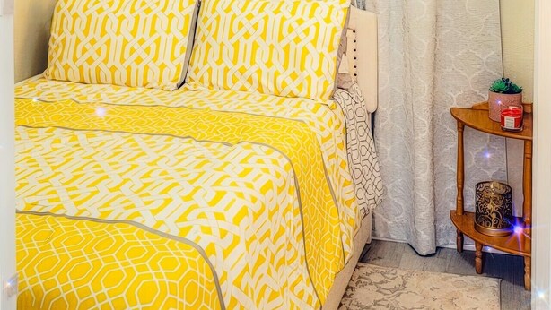 A bedroom with a bed, curtains, a bedside table with a candle, and a patterned rug. - The Blue Sunshine Retreat (Citra)