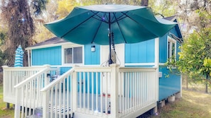 Ein blaues Haus mit weißer Veranda, einem großen Sonnenschirm und einem kleinen Baum im Hintergrund.