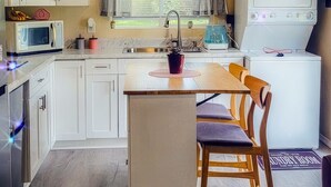 A compact kitchen with white cabinets, a central island, a microwave, a sink, and a stove. - The Blue Sunshine Retreat (Citra)