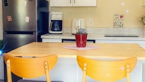 A kitchen with a central island, two wooden chairs with cushioned seats, a coffee maker, a refrigerator, and a sign on the wall. - The Blue Sunshine Retreat (Citra)
