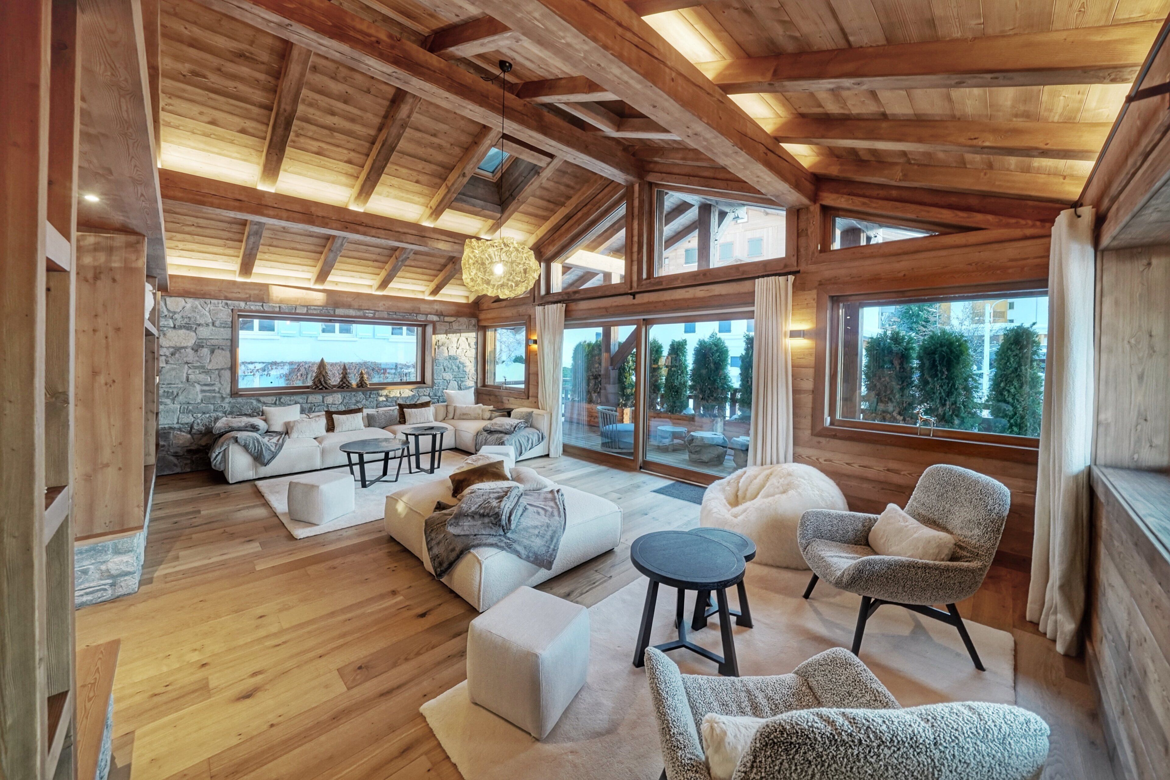 A spacious living area with a stone fireplace, wooden beams, and large windows offering views of the outdoors.