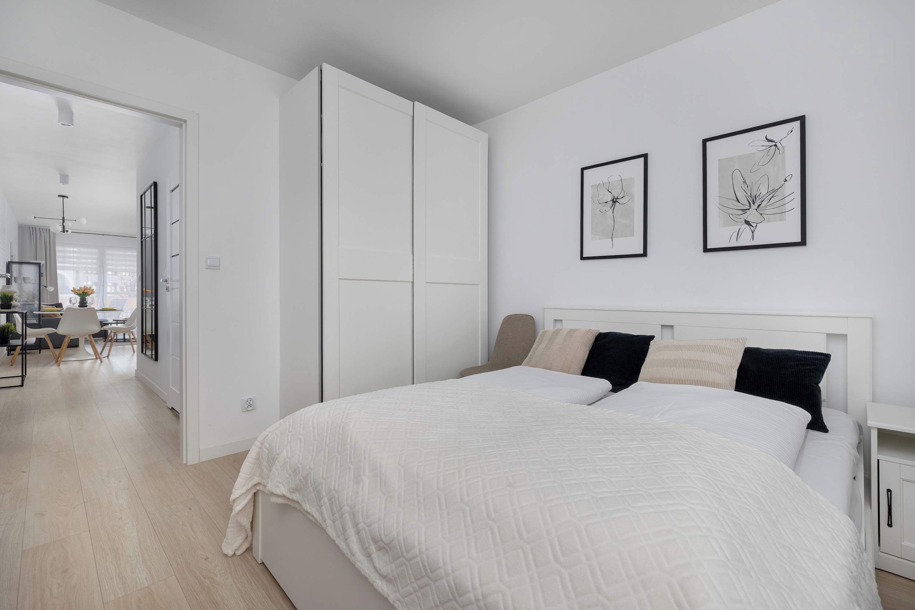 Ein Schlafzimmer mit einem Bett, einem Kleiderschrank und zwei gerahmten Kunstwerken an der Wand.