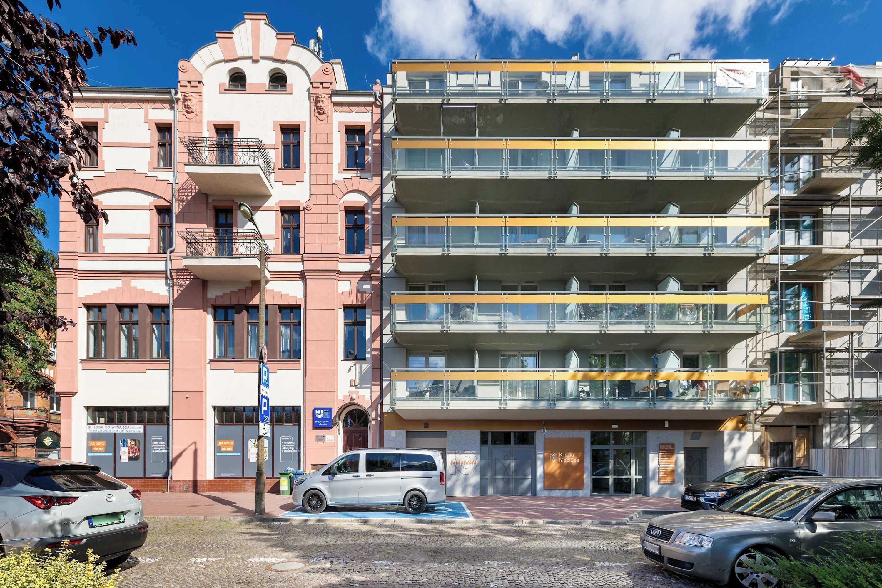Ein mehrgeschossiges Gebäude mit einer Mischung aus Baustilen, darunter eine rosa Fassade mit klassischer Gestaltung und ein moderner Glasbau.