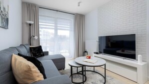 Ein modernes Wohnzimmer mit grauem Sofa, rundem Couchtisch, Flachbildfernseher und einer Wand aus weißen Ziegelsteinen.