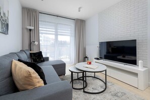 A modern living room with a grey sofa, a round coffee table, a flat-screen TV, and a white brick wall. - Modern Apartment with a Balcony | City Centre (Świnoujście)