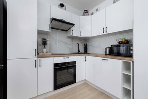 Eine moderne Küche mit weißen Schränken, einem Einbauofen, einer Kaffeemaschine und einer Obstschale auf der Arbeitsplatte.