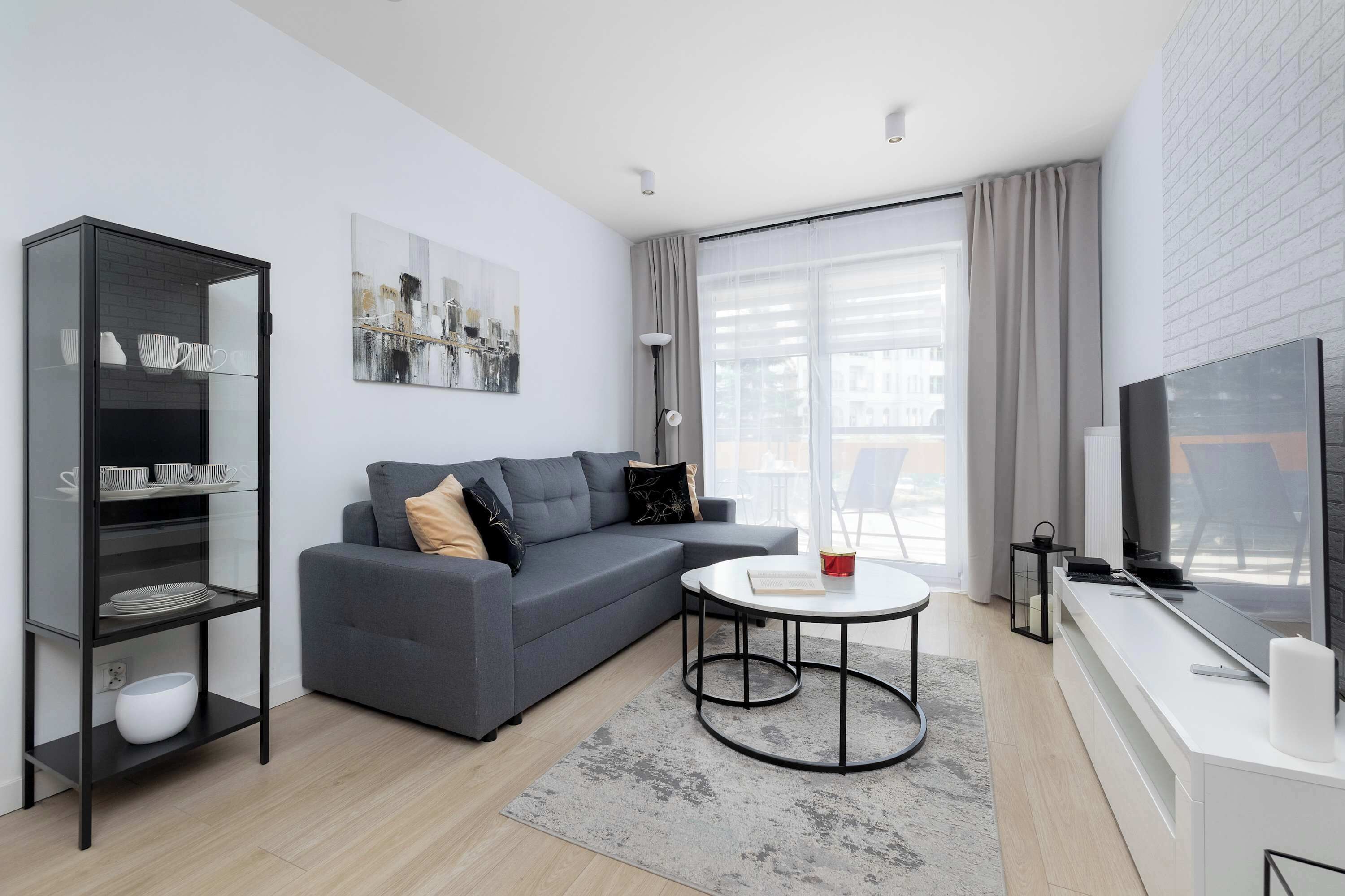 Ein modernes Wohnzimmer mit einem grauen Sofa, einer Glaskabine, einem runden Couchtisch und einem Flachbildfernseher.