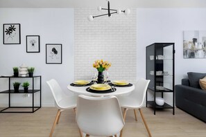 A modern dining area with a white table set for four, surrounded by white chairs. - Modern Apartment with a Balcony | City Centre (Świnoujście)