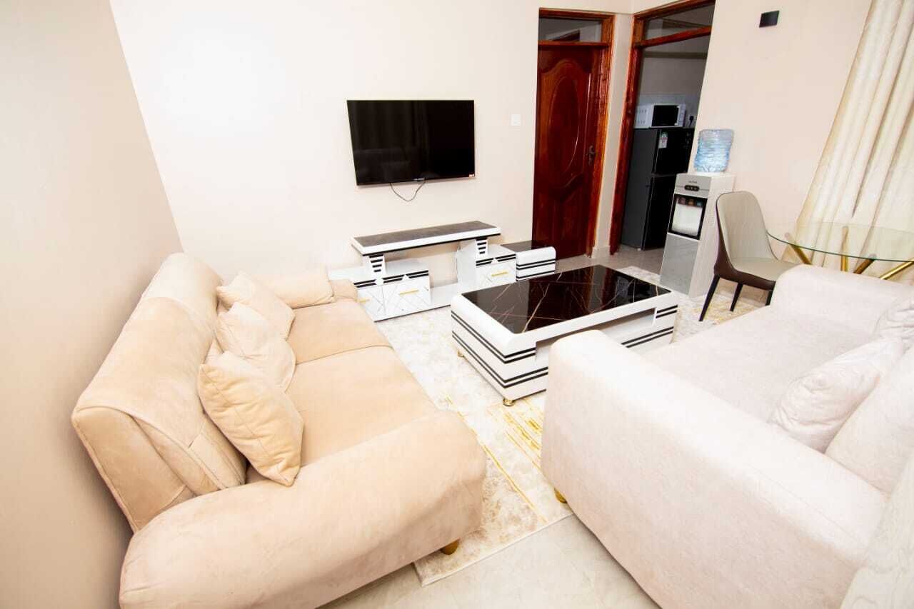 Uma sala de estar com sofá, mesa de centro, TV e pequena área de cozinha com micro-ondas.