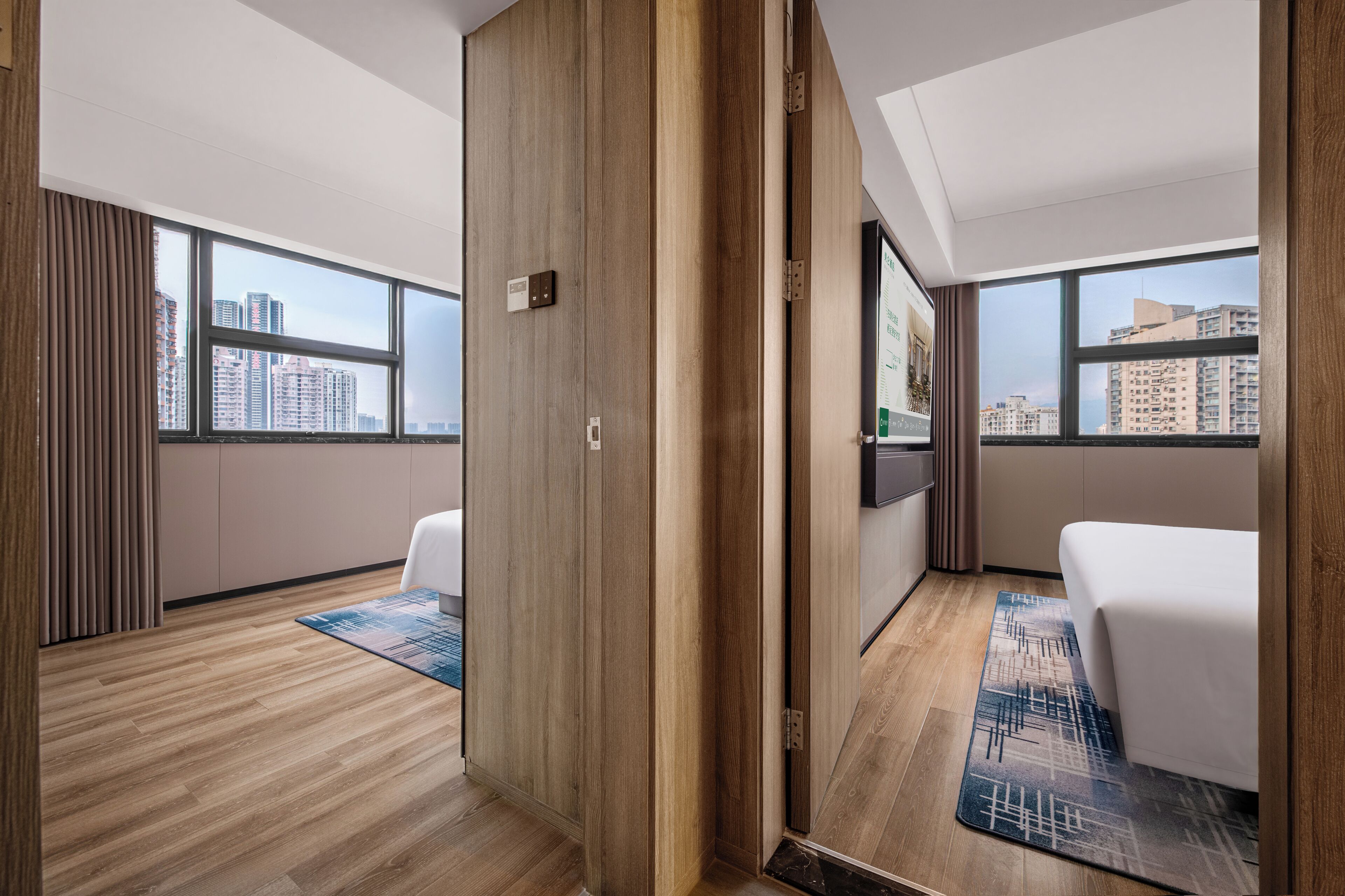 Habitación de hotel con piso de madera, una cama, un escritorio y vistas de la ciudad a través de amplias ventanas.