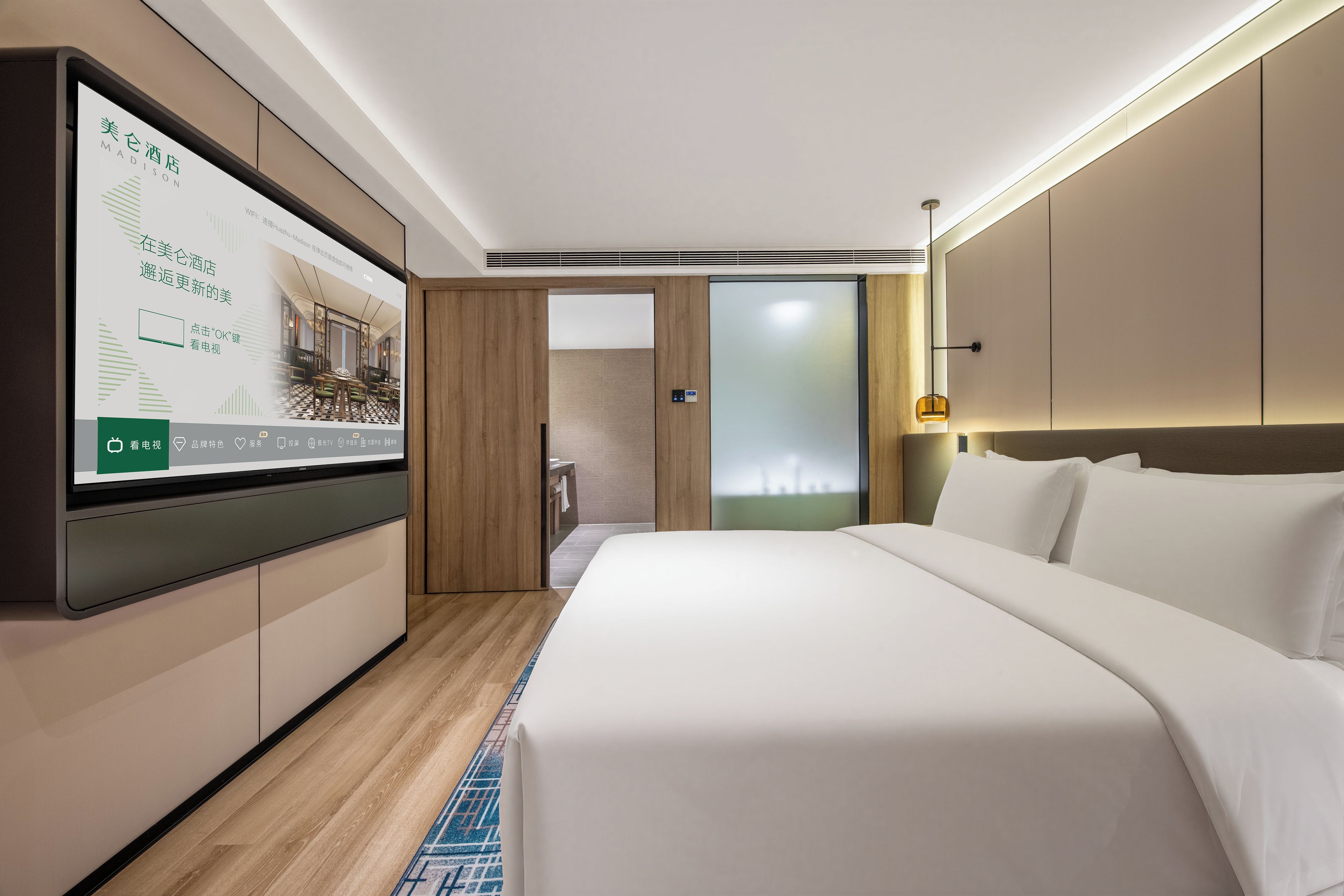 A hotel room with a bed, a television displaying a room layout, and a bathroom visible through a door.