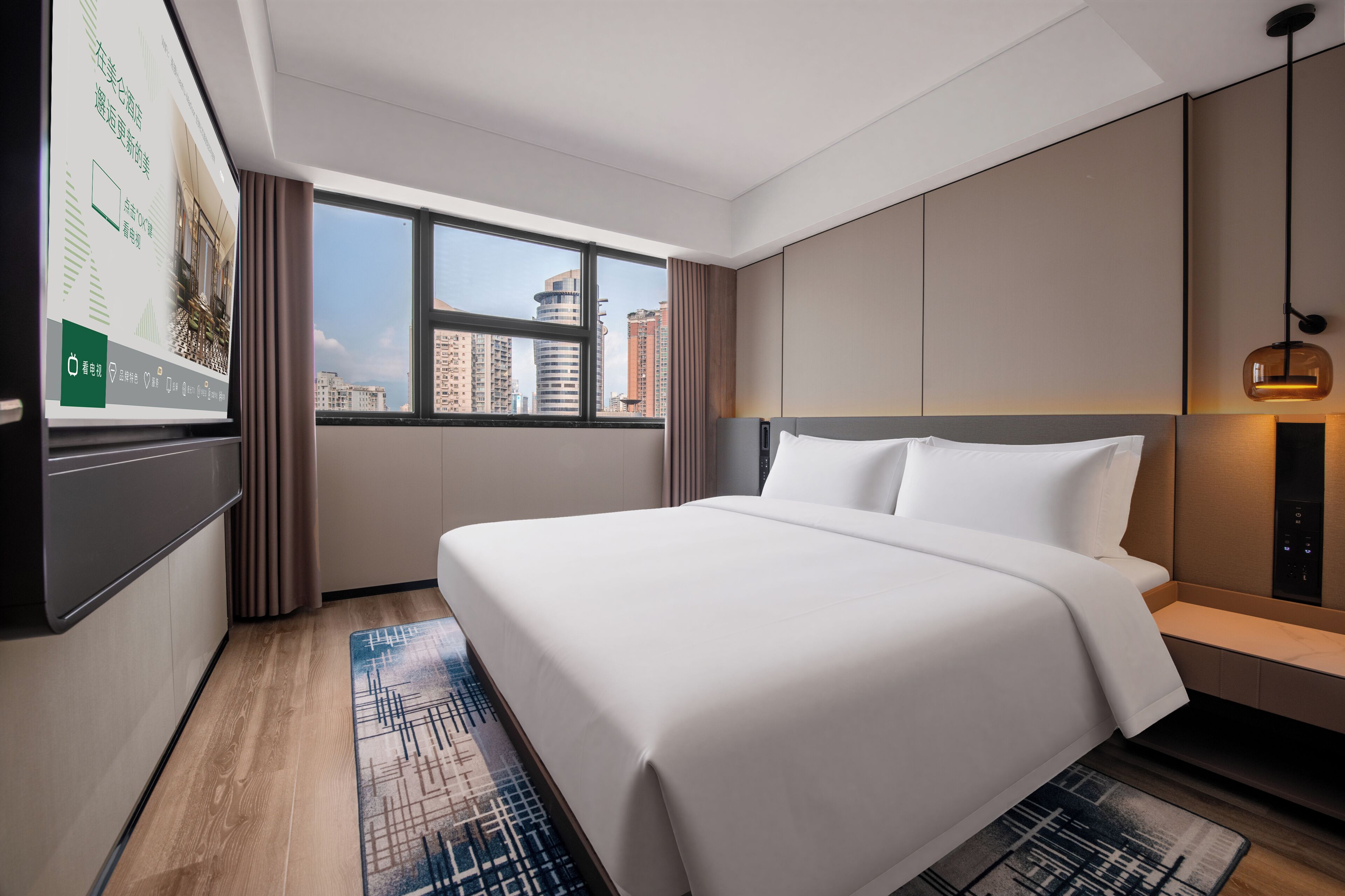 A hotel room with a large bed, a view of the cityscape through the window, and a flat-screen TV mounted on the wall.