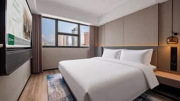 A hotel room with a large bed, a view of the cityscape through the window, and a flat-screen TV mounted on the wall.