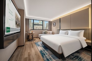 Ein Hotelzimmer mit einem großen Bett, einem Schreibtisch mit Stuhl, einem Fernseher und Blick auf die Stadt durch das Fenster.