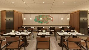 Un restaurant amb diverses taules i cadires, un mural gran a la paret i llums penjants.