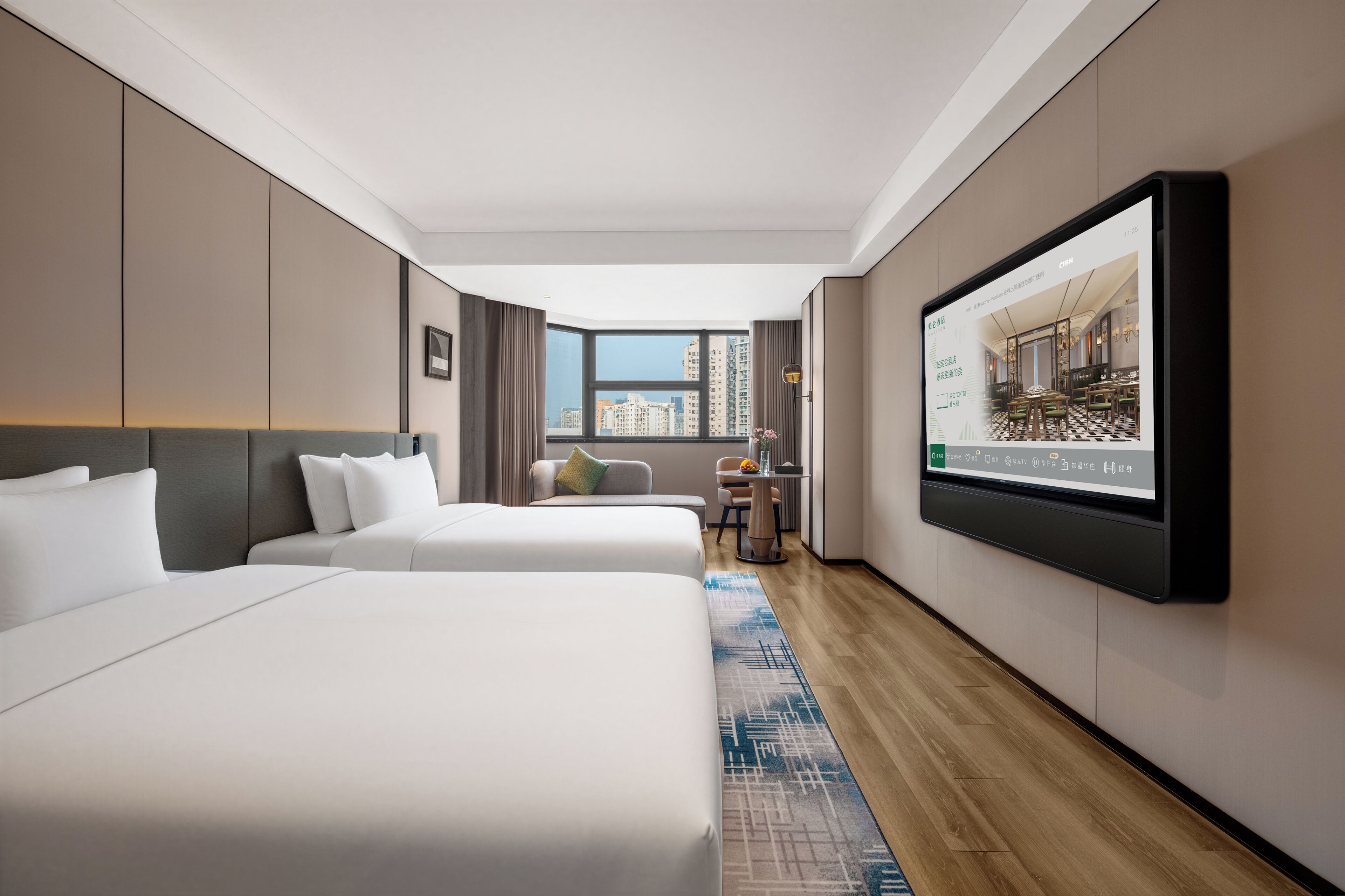 Quarto de hotel com duas camas, TV fixada na parede, janela vista para a cidade e uma pequena mesa com uma cadeira.